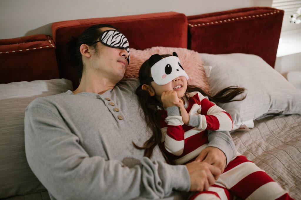 A father and daughter wearing sleep masks relax on a cozy bed, enjoying a moment together.